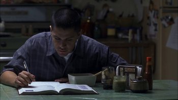 Movie still from “Crazy/Beautiful” (2001), directed by John Stockwell – A man sitting at a table with a bowl of food and a book; Medium shot, High angle