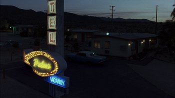 Movie still from “Crazy/Beautiful” (2001), directed by John Stockwell – A motel sign lit up at night with a car parked on the side of the road; Extreme Wide shot, High angle