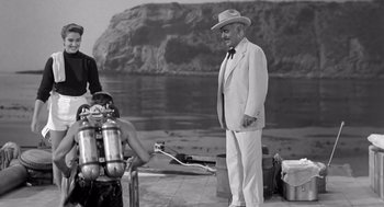 Movie still from “Creature from the Black Lagoon” (1954), directed by Jack Arnold – An older man wearing a suit and a hat standing next to a woman; Medium shot, Over the shoulder angle