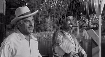 Movie still from “Creature from the Black Lagoon” (1954), directed by Jack Arnold – A black - and - white photo of two men sitting next to a body of water; Medium shot, Low angle