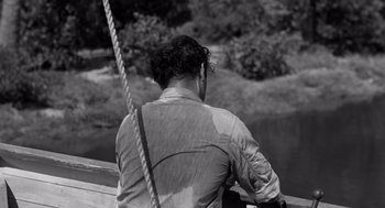 Movie still from “Creature from the Black Lagoon” (1954), directed by Jack Arnold – A black and white photo of a man sitting on a bridge; Medium shot, High angle