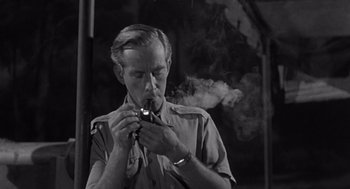 Movie still from “Creature from the Black Lagoon” (1954), directed by Jack Arnold – A man smoking a pipe while wearing a military uniform; Close Up shot, High angle