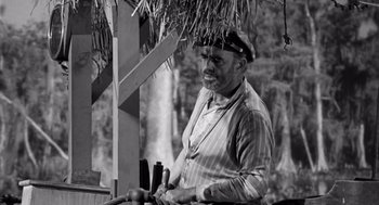 Movie still from “Creature from the Black Lagoon” (1954), directed by Jack Arnold – An old man is working on a piece of wood; Medium shot, Low angle