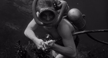 Movie still from “Creature from the Black Lagoon” (1954), directed by Jack Arnold – A man in a diving suit is holding his hands out; Medium shot, High angle