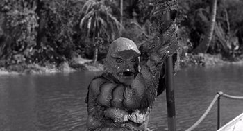 Movie still from “Creature from the Black Lagoon” (1954), directed by Jack Arnold – A man in a gorilla suit holding a pole in a body of water; Medium shot, High angle