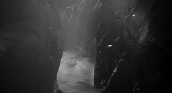 Movie still from “Creature from the Black Lagoon” (1954), directed by Jack Arnold – A black and white photo of a cave with smoke coming out of it; Extreme Wide shot, High angle
