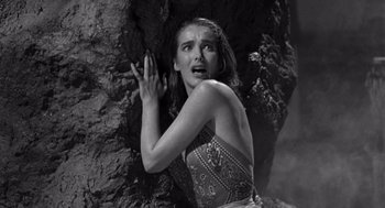 Movie still from “Creature from the Black Lagoon” (1954), directed by Jack Arnold – A woman in a dress is climbing on a rock wall; Medium shot, High angle