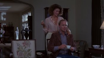 Movie still from “Creepshow” (1982), directed by George A. Romero – A man sitting in front of a woman holding a cup; Medium shot, Low angle