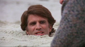 Movie still from “Creepshow” (1982), directed by George A. Romero – A man with a long hair is laying in the sand; Close Up shot, High angle