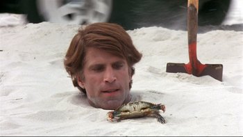 Movie still from “Creepshow” (1982), directed by George A. Romero – A man in the sand with a crab in his hand; Close Up shot, High angle