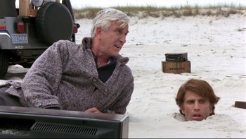 Movie still from “Creepshow” (1982), directed by George A. Romero – A man sitting on top of a television in the sand; Medium shot, Over the shoulder angle
