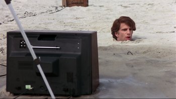 Movie still from “Creepshow” (1982), directed by George A. Romero – A man in the middle of the sand looking at a tv; Wide shot, High angle