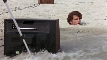 Movie still from “Creepshow” (1982), directed by George A. Romero – A man in the sand looking at a television; Wide shot, High angle
