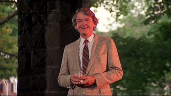 Movie still from “Creepshow” (1982), directed by George A. Romero – A man in a suit and tie holding a glass of wine; Medium shot, Low angle