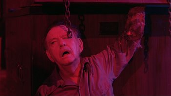 Movie still from “Creepshow” (1982), directed by George A. Romero – A man hanging from a metal chain in a dark room; Close Up shot, Low angle