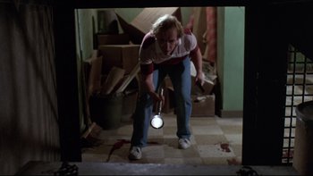 Movie still from “Creepshow” (1982), directed by George A. Romero – A woman is holding a flashlight in a room; Medium shot, High angle