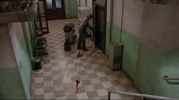 Movie still from “Creepshow” (1982), directed by George A. Romero – A man sweeping the floor of a room with blood on the floor; Wide shot, High angle