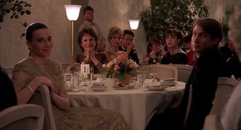 Movie still from “Crimes and Misdemeanors” (1989), directed by Woody Allen – A group of people sitting at a table with flowers; Medium shot, Over the shoulder angle