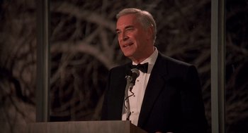 Movie still from “Crimes and Misdemeanors” (1989), directed by Woody Allen – A man in a tuxedo is speaking at a podium; Close Up shot, Low angle