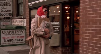 Movie still from “Crimes and Misdemeanors” (1989), directed by Woody Allen – A woman walking down the street with a bunch of newspapers in her hands; Medium shot, Low angle