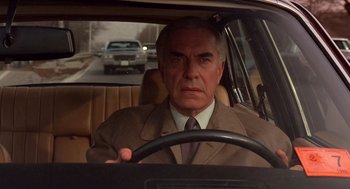 Movie still from “Crimes and Misdemeanors” (1989), directed by Woody Allen – An older man in a suit and tie driving a car; Close Up shot, Low angle