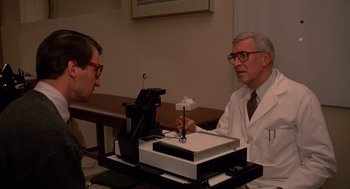 Movie still from “Crimes and Misdemeanors” (1989), directed by Woody Allen – An older man in a white lab coat is talking to an older man in glasses; Medium shot, Low angle