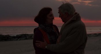 Movie still from “Crimes and Misdemeanors” (1989), directed by Woody Allen – An older man and a younger woman embracing on the beach at sunset; Medium shot, Low angle