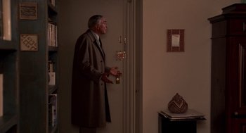 Movie still from “Crimes and Misdemeanors” (1989), directed by Woody Allen – An older man wearing a long coat standing at the entrance of a room; Medium shot, High angle