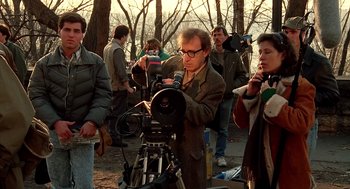 Movie still from “Crimes and Misdemeanors” (1989), directed by Woody Allen – A group of people standing in a park with a camera; Medium shot, Over the shoulder angle