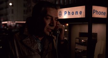 Movie still from “Crimes and Misdemeanors” (1989), directed by Woody Allen – A man talking on a phone in front of a phone booth; Close Up shot, High angle