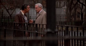 Movie still from “Crimes and Misdemeanors” (1989), directed by Woody Allen – Two older men standing next to each other near a metal fence; Medium shot, Over the shoulder angle