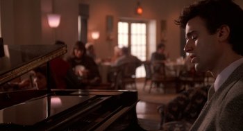 Movie still from “Crimes and Misdemeanors” (1989), directed by Woody Allen – A person playing a piano in a room with people; Close Up shot, Over the shoulder angle