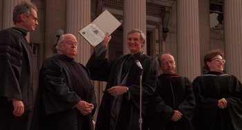 Movie still from “Crimes and Misdemeanors” (1989), directed by Woody Allen – A man holding up a diploma in front of three other men; Medium shot, High angle