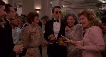 Movie still from “Crimes and Misdemeanors” (1989), directed by Woody Allen – A man in a tuxedo surrounded by women in formal wear; Medium shot, Low angle