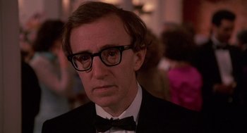 Movie still from “Crimes and Misdemeanors” (1989), directed by Woody Allen – A person wearing a suit and glasses; Close Up shot, Over the shoulder angle