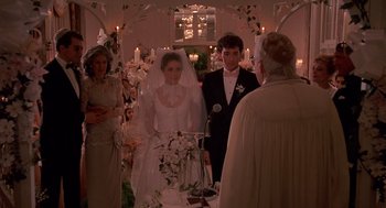 Movie still from “Crimes and Misdemeanors” (1989), directed by Woody Allen – A bride and groom standing in front of a priest in front of a wedding arch; Medium shot, Over the shoulder angle