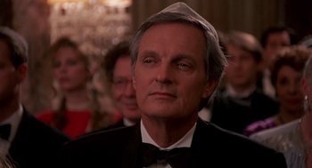 Movie still from “Crimes and Misdemeanors” (1989), directed by Woody Allen – A person wearing a suit and bow tie; Close Up shot, Over the shoulder angle