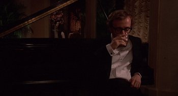 Movie still from “Crimes and Misdemeanors” (1989), directed by Woody Allen – A man sitting at a piano drinking a glass of wine; Medium shot, Over the shoulder angle