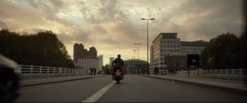 Movie still from “Criminal” (2016), directed by Ariel Vromen – A man riding a motorcycle down a street; Extreme Wide shot, Low angle