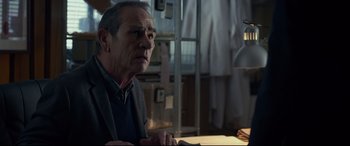 Movie still from “Criminal” (2016), directed by Ariel Vromen – An older man sitting at a table in front of a lamp; Close Up shot, Over the shoulder angle
