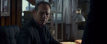 Movie still from “Criminal” (2016), directed by Ariel Vromen – An older man sitting at a table in front of a lamp; Close Up shot, Over the shoulder angle