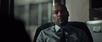 Movie still from “Criminal” (2016), directed by Ariel Vromen – A man sitting in an office chair wearing a tie; Close Up shot, Over the shoulder angle
