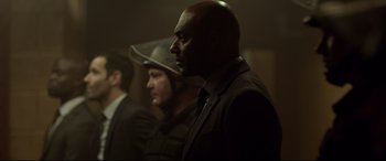 Movie still from “Criminal” (2016), directed by Ariel Vromen – A man in a suit and a cowboy hat is standing next to another man in a suit; Medium shot, Over the shoulder angle