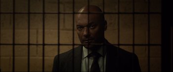 Movie still from “Criminal” (2016), directed by Ariel Vromen – A man in a suit and tie behind bars looking straight ahead; Close Up shot, Over the shoulder angle