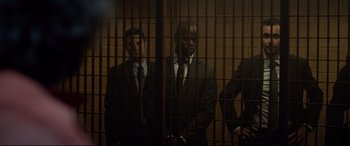 Movie still from “Criminal” (2016), directed by Ariel Vromen – A group of men standing next to each other in front of bars; Medium shot, Low angle