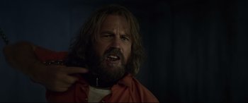 Movie still from “Criminal” (2016), directed by Ariel Vromen – A man with long hair and a beard is looking angry; Close Up shot, Over the shoulder angle
