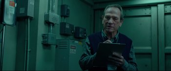 Movie still from “Criminal” (2016), directed by Ariel Vromen – An older man holding a tablet in a room; Medium shot, Low angle