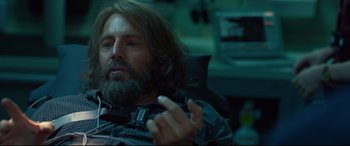 Movie still from “Criminal” (2016), directed by Ariel Vromen – A man with long hair and beard sitting in a chair; Close Up shot, Over the shoulder angle