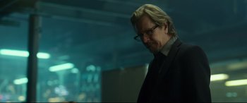 Movie still from “Criminal” (2016), directed by Ariel Vromen – A person wearing a suit and glasses; Close Up shot, Over the shoulder angle