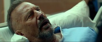 Movie still from “Criminal” (2016), directed by Ariel Vromen – An older man laying in a hospital bed with his mouth open; Close Up shot, Over the shoulder angle